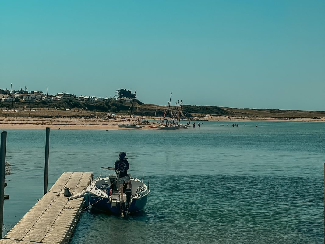 Ponton et petit voilier sur la Ria d'Étel, plage à voile et dunes en arrière-plan